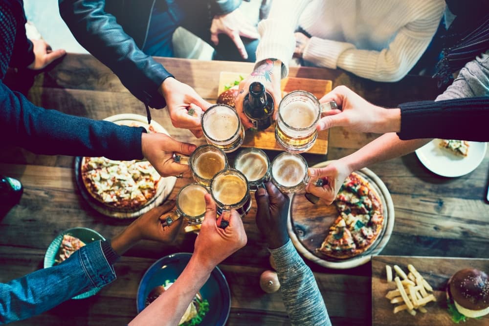 A group of people at a restaurant with pizza on the table, toasting with beer glasses