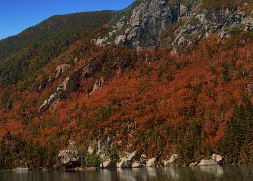 Autumn foliage reflects on a calm lake surrounded by rocky mountains. Autumn foliage reflects on a calm lake surrounded by rocky mountains.