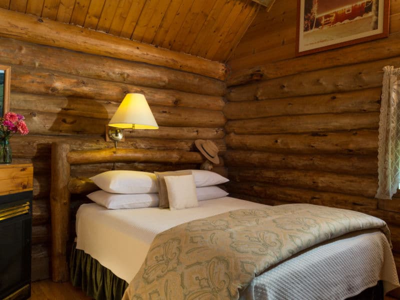 Queen bed with log headboard and reading lamp above, gas fireplace, and window facing east.