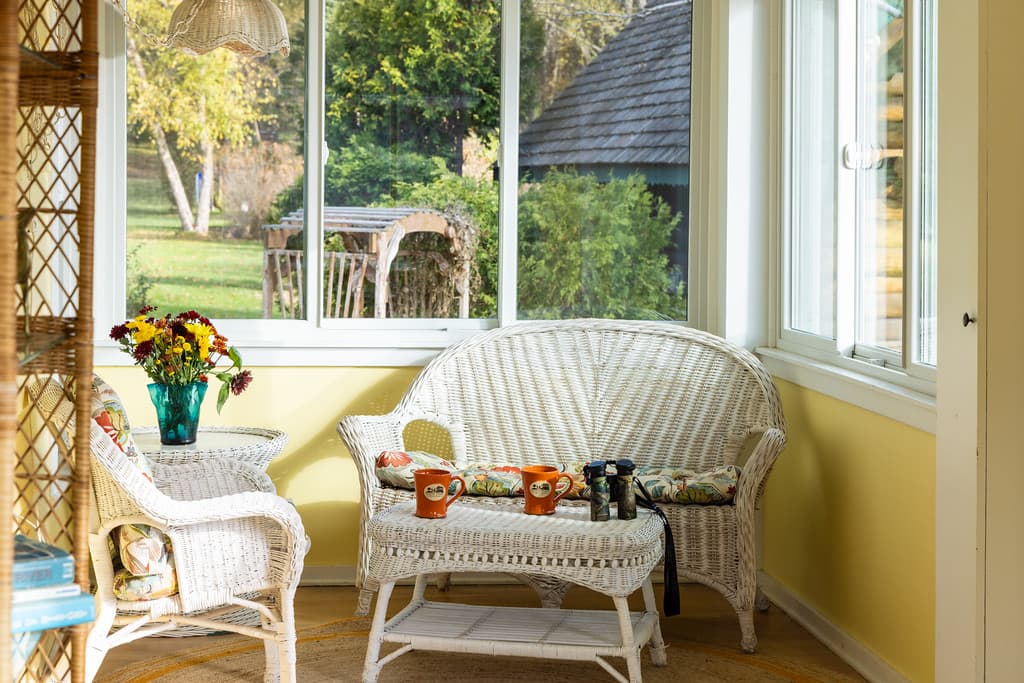A white wicker furniture set with floral cushions invites you to sit awhile on the porch with windows on three sides.