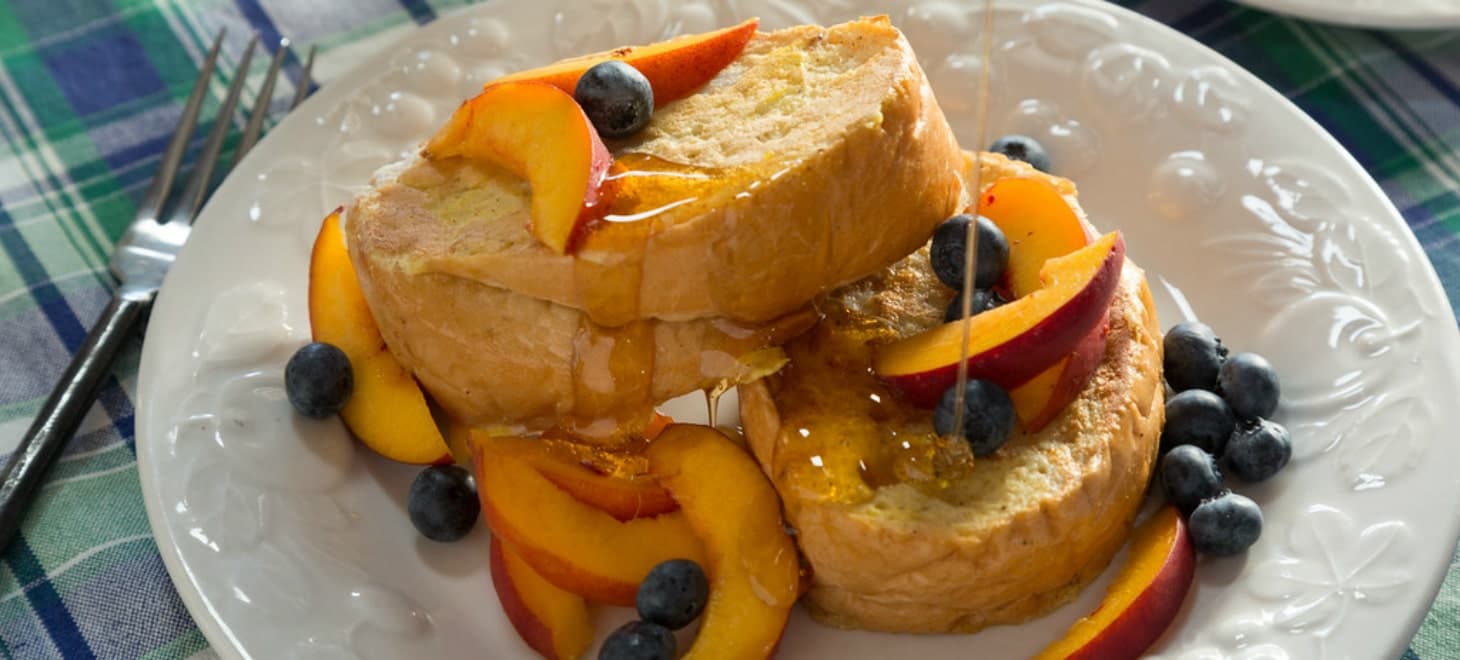 A plate with french toast topped with blueberries and peaches, drizzled with maple syrup
