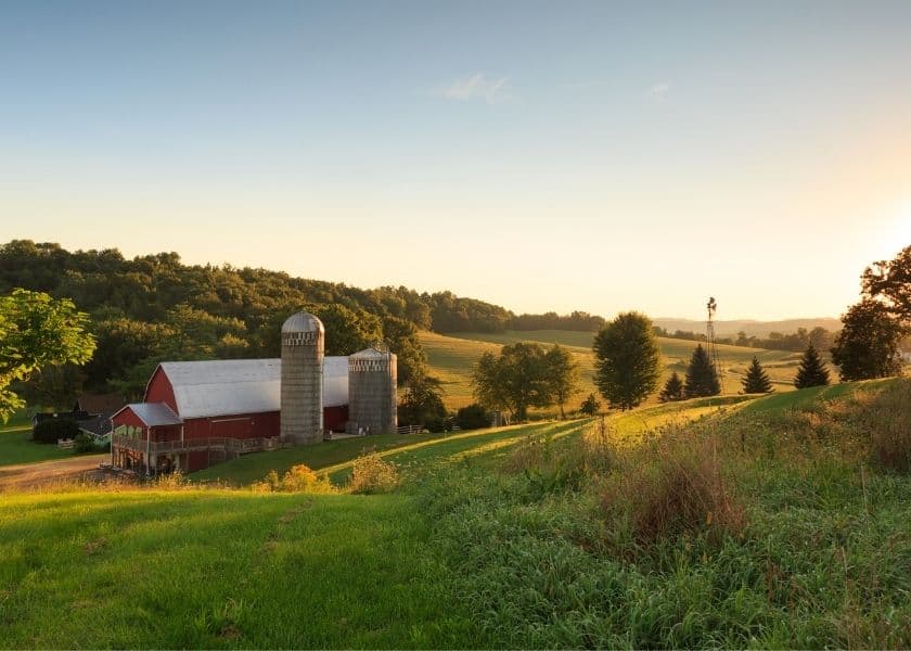 Red barn and silos at Justin Trails surrounded by rolling Driftless Region hills, prairie grasses, woods, and sunrise light. Red barn and silos at Justin Trails surrounded by rolling Driftless Region hills, prairie grasses, woods, and sunrise light.